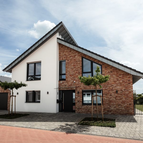 Modernes Einfamilienhaus der gebaut von der Bauunternehmung Brouwer mit weißer Putzfassade und rotem Klinker, großen Fenstern, Satteldach und gepflegtem Vorgarten unter blauem Himmel.